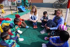 Nepal Two Care & Community volunteers in Nepal sit in a circle with local children, preparing to play an educational game.