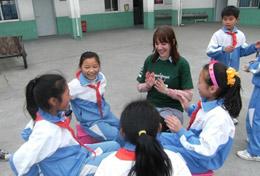 Care A high school volunteer sits in a playground in China with local children, playing an educational game with them.