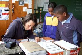South Africa Two school children watch as a Teaching volunteer demonstrates how to complete the English homework assigned to them.